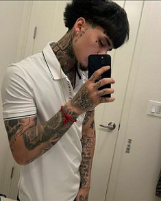 a man with tattoos taking a selfie in front of a mirror while wearing a white polo shirt