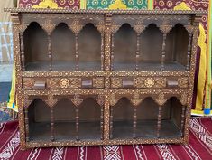 an old wooden cabinet with intricate carvings on the front and sides, sitting on a rug