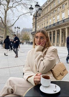 a woman sitting at a table with a cup of coffee in front of her on the street