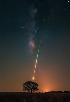 an object is flying high in the sky above a tree and grass field at night