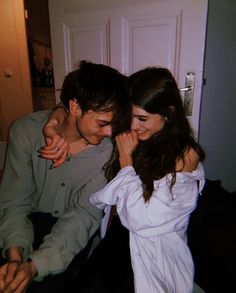 a man and woman standing next to each other in front of a white door with an electronic device