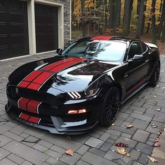 a black car with red stripes parked in front of a garage on a brick driveway