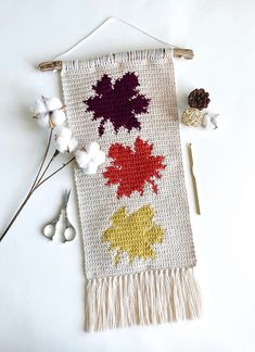 a knitted wall hanging with flowers and scissors on it next to cotton floss