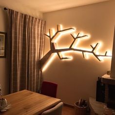 a living room with a table, chairs and a tree branch light up the wall