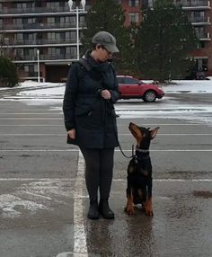 a woman standing next to a dog on a leash in the street with buildings behind her