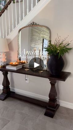 a table with a mirror, vase and candles on it in front of a stair case