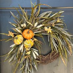 a wreath with flowers and pumpkins hanging on the front door