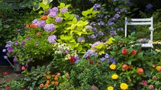 a garden filled with lots of colorful flowers next to a white chair in the middle