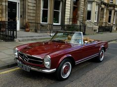 an old red convertible car is parked on the street