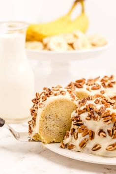 a white plate topped with a cake covered in frosting and nuts next to a glass of milk