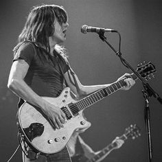 a man with long hair playing guitar in front of a microphone and singing into a mic