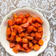 a white bowl filled with chopped carrots on top of a lace tablecloth covered table