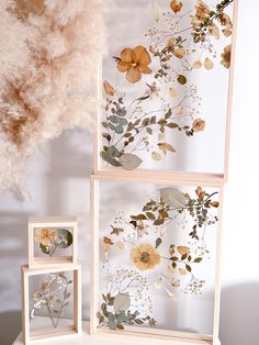 three wooden frames with pressed flowers and leaves in them on a white table next to a dried flower arrangement