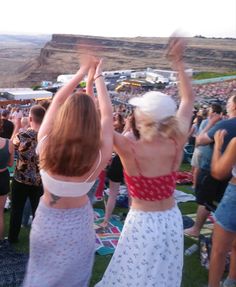 two women in dresses are dancing at an outdoor music festival with their hands up to the sky