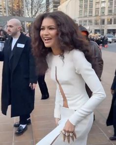 a woman in a white dress is walking down the street with her hand on her hip