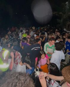 a large group of people standing around each other at a concert or party with lights on