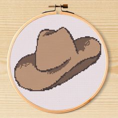 a cross stitch pattern with a brown cowboy hat on it's side, in front of a wooden background