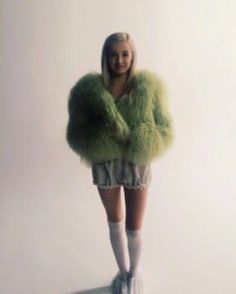 a woman in short shorts and green fur coat posing for the camera with her hands on her hips