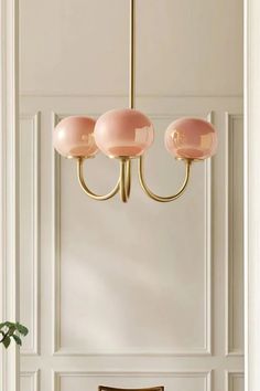 a dining room table and chairs in front of a white wall with pink lamps hanging from the ceiling