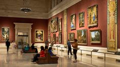 people are looking at paintings on display in a large room with marble floors and red walls