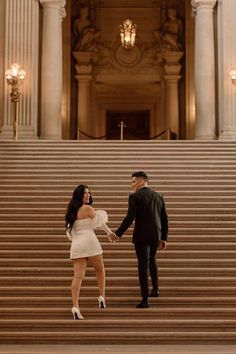 a man and woman are standing on the steps in front of a building holding hands