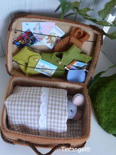 an open suitcase filled with baby items on top of a white table next to a potted plant