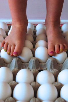 a woman's feet standing on top of an egg carton filled with white eggs