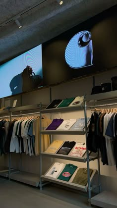 a display in a clothing store filled with lots of shirts and ties on racks next to a large screen