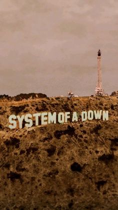 there is a sign that says system of a down on top of a hill with a lighthouse in the background