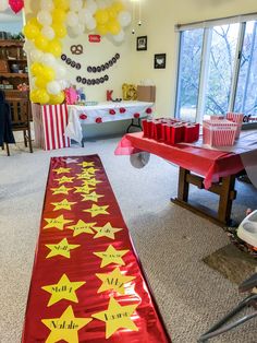 a long red table with yellow stars on it in a room filled with balloons and other decorations