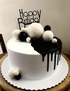 a white and black birthday cake with pom - poms on the top is sitting on a wooden table