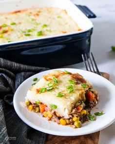 a white plate topped with lasagna next to a casserole dish