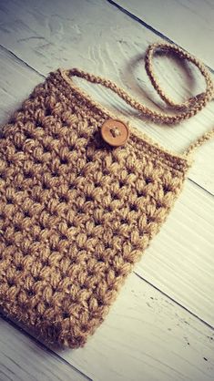 a crocheted bag with a wooden button on the front is laying on a white wood floor