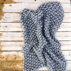 a gray knitted scarf laying on top of a wooden floor next to a piece of wood