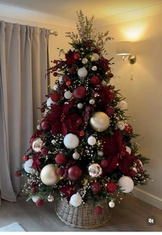 a christmas tree decorated with red, white and silver ornaments in a basket next to a window