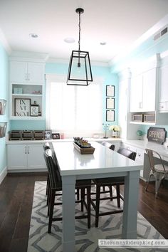 a kitchen with blue walls and white cabinets, an island in the center is surrounded by black chairs