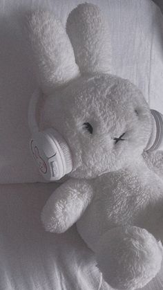 a white stuffed animal laying on top of a bed with headphones in it's ears