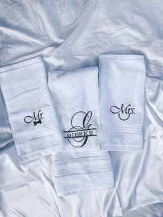 three white towels with embroidered logos on them sitting on top of a sheeted bed