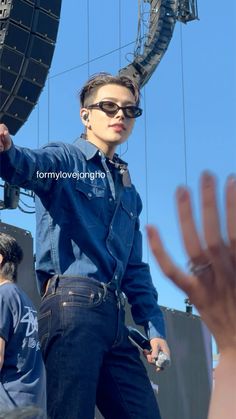 a man with sunglasses on standing in front of a stage holding his hand up to the sky