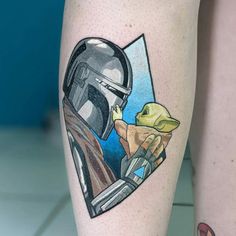 a star wars tattoo on the leg of a person wearing a helmet and holding a baby yoda