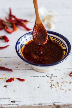 a spoon full of chili sauce on top of a white table with red peppers scattered around it