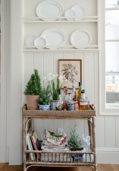 a wicker shelf with plates and plants on it in front of a white wall