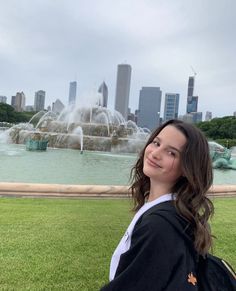 a woman standing in front of a fountain with the city skyline in the back ground