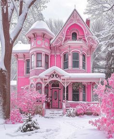 a pink victorian house with snow on the ground and trees in front of it,