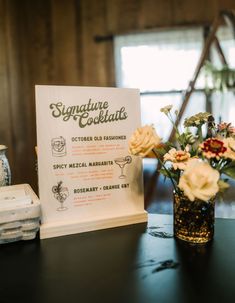 there is a sign that says signature cocktails next to a vase with flowers in it