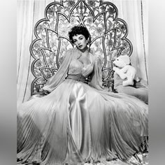 a woman in a long dress sitting on a chair with a teddy bear next to her