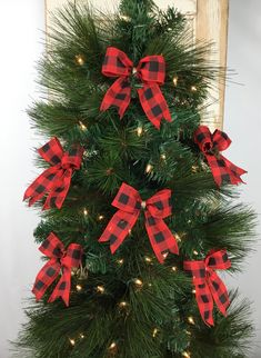 a christmas tree decorated with red and black plaid ribbon bows, lights and pine needles