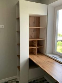 an empty room with a window and some shelves in the corner, next to a desk