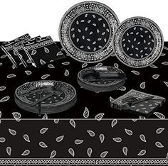 a table topped with black and white plates covered in paisley print cloth next to silverware