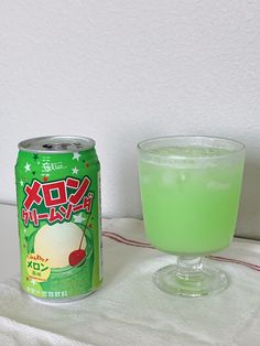 a can of soda next to a glass filled with green liquid on a white table